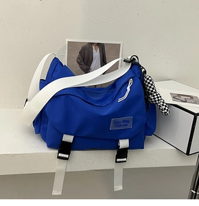 Close-up of blue nylon crossbody bag with white buckle strap and checkered charm detail