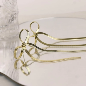 Detail of golden bow-knot tassel earrings with snake chain on a reflective mirror surface