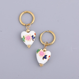 Detail of heart-shaped ceramic earrings with colorful floral hand-painted pattern on gold hoop