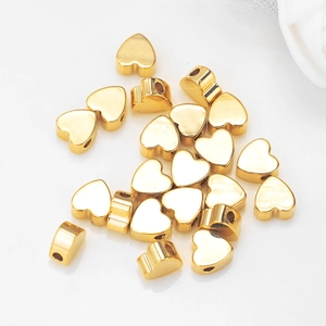 Polished gold heart beads scattering on white reflective surface for DIY jewelry making