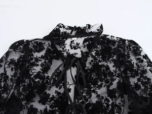 Close-up of black mesh blouse with floral flocking and tie-neck detail on white background