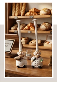 Close-up of resin chef figurines with tall hats holding bread and wine on a bakery counter