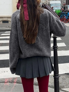 Street style view of grey knit sweater paired with pleated skirt and burgundy tights