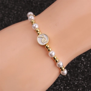 Perlenarmband mit goldenen Perlen und einem runden Buchstabenanhänger am Handgelenk