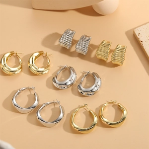 Set of gold and silver metallic C-shaped and textured hoop earrings on beige background