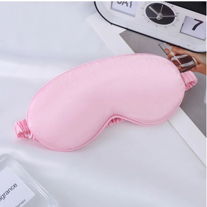Pink silk sleep mask with elastic strap shown with lifestyle accessories for travel