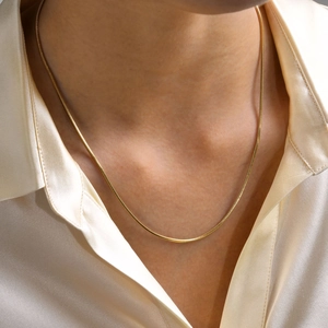 Close-up of a gold square snake bone chain necklace worn over a beige silk shirt