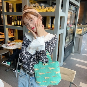 Detail of light green printed canvas lunch bag held by a model in a floral shirt