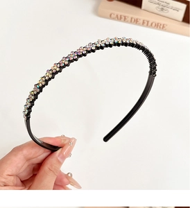 Close-up of a slim black headband with rainbow rhinestones held by a hand on a desk