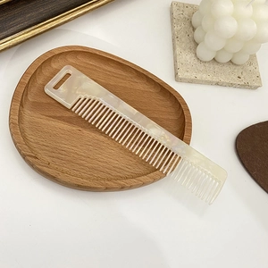 Detail of cream marble acetate hair comb with wide teeth on a minimalist wooden tray