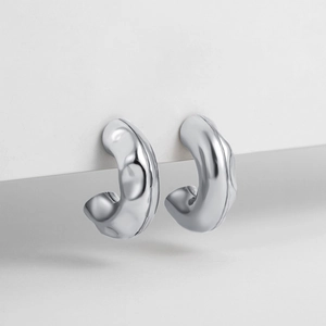 Macro detail of silver C-shaped earrings with hammered liquid metal texture and glossy finish