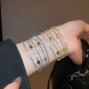 Detail of layered rhinestone bracelets with heart charms in gold and silver finish