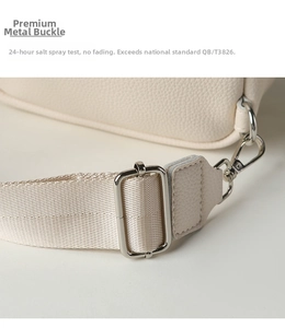 Detail of silver metal lobster clasp and textured beige leather strap on crossbody bag
