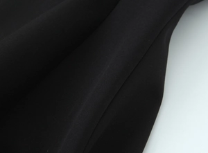 Close-up of the black fabric's fine woven texture and smooth quality on this romper