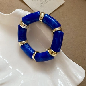 Macro detail of blue marble acetate segments and gold spacer beads on elastic bracelet
