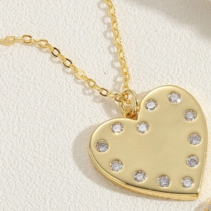 Macro shot of gold heart pendant featuring polished surface and sparkling zircon border