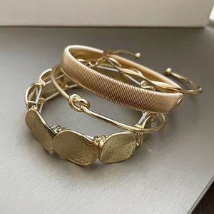 Macro detail of a four-piece gold bracelet set featuring twisted and hammered textures