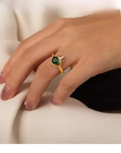 Dettaglio di un anello dorato con zircone verde a cuore e accenti a corona sulla mano