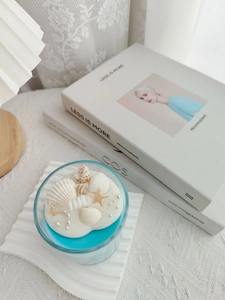 Close-up of ocean-themed soy candle with blue wax, shells, and starfish in a glass cup