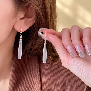 Detail of elegant gold drop earrings with white teardrop stones and pearl accents