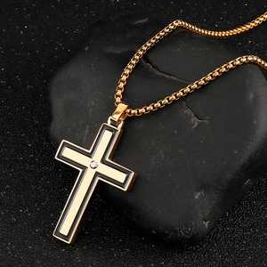Detailed close-up of golden cross pendant with black enamel inlay on a textured stone