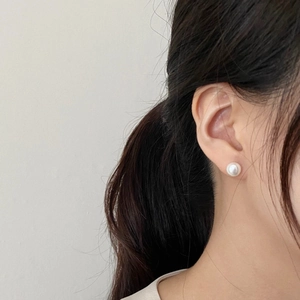 Detail of high-luster white pearl stud earrings shown worn on a model in a minimalist style