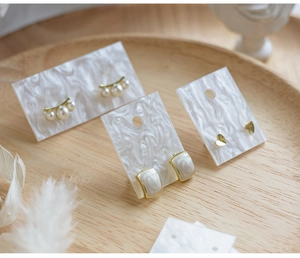 Detail of pearl and heart stud earrings set displayed on white marble cards and wooden tray