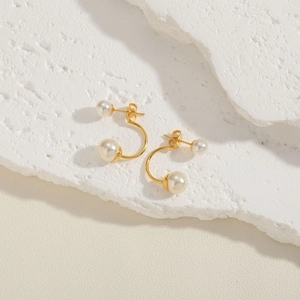 Macro view of gold C-shaped earrings with white pearls on a textured white stone
