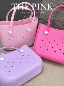 Three colorful EVA beach tote bags in pink, rose, and purple with signature cutout holes
