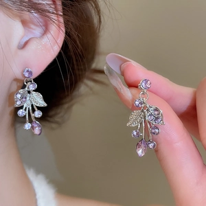 Macro detail of silver grape-shaped earrings with purple crystals and leaf metal design