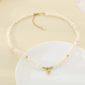 Dettaglio di una collana di perle vintage con ciondolo a sfera dorata su sfondo beige
