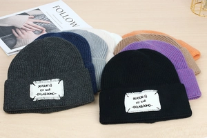 Detail of colorful knit beanies with vintage patch label on wooden background