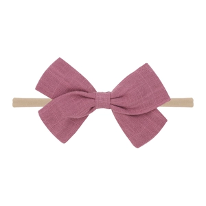 Detail of a soft pink fabric bow on a beige elastic nylon baby headband on white background