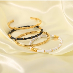 Detail of bamboo shaped stackable gold bangles with black and white enamel on satin