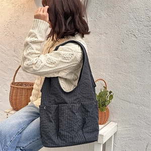 Detail of grey plaid shoulder bag featuring front pockets and metallic buckles