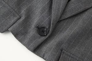 Gros plan d'un bouton noir à quatre trous sur le tissu texturé gris foncé du gilet