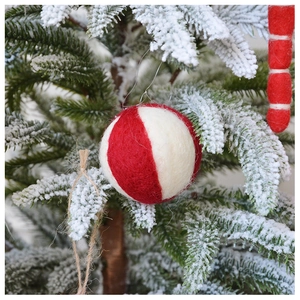 Detail of red and white striped handmade wool felt ball hanging on a snowy Christmas tree