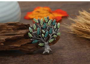 Detail of tree of life brooch with green and blue crystals on dark wood with autumn leaves