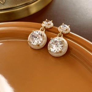 Detailed close-up of gold drop earrings with white enamel and large sparkling crystals