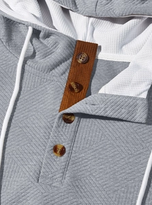 Détail d'un sweat à capuche gris gaufré avec patte de boutonnage marron et boutons