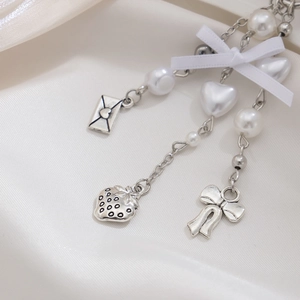 Detail of silver strawberry and bow charms with pearls on white silk background