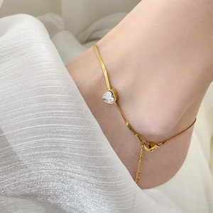 Detail of a gold snake chain anklet with a heart-shaped zircon on a model's ankle