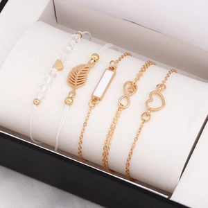 Detail of five-piece gold bracelet set with leaf and heart charms on a jewelry cushion