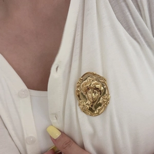 Broche visage vintage en or mat avec un design de portrait sur un cardigan blanc