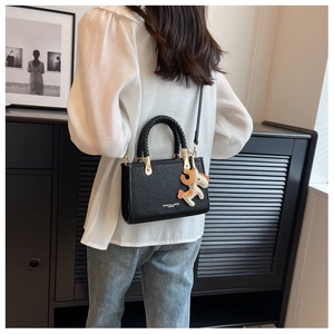 Chic black bucket bag with woven handle and horse charm shown on model in modern setting