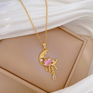 Detail of gold moon necklace with pink heart gem and crystal drop on silk fabric