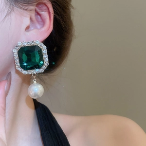 Detail of elegant emerald-cut green gemstone earring with large white pearl drop