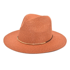 Detail of terracotta woven straw hat featuring black band and golden metal buckle accent