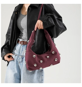 Detail of burgundy tote bag with silver studs and wide strap in a modern punk style