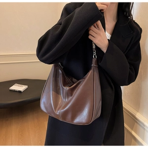 Detail of dark brown retro underarm bag with white stitching and silver metal chain strap